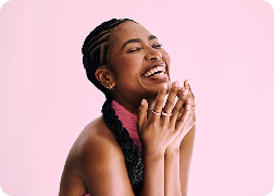 A young black woman smiling with a pink background.