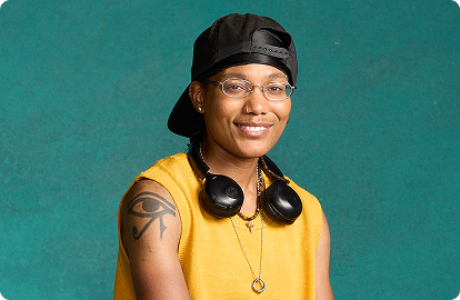 A person in a backwards hat with headphones around their neck smiling.